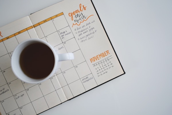 White tabletop, calendar, cup of coffee, nicholas fainlight managing your schedule as young professional