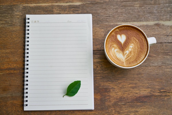 Blank white piece of paper with a small leaf on it, cup of coffee next to it, both on a table, Nicholas Fainlight blog about how to develop a great morning routine