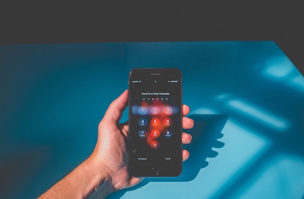 Person's hand holding a locked phone above a blue background, Nicholas Fainlight keep financial accounts secure